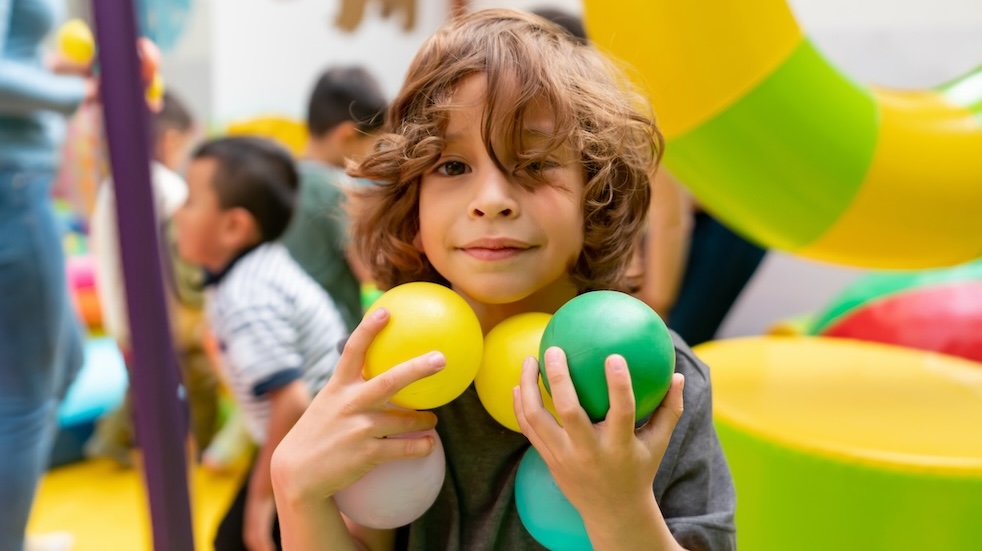 Portrait of a happy boy playing with balls at the playground and looking at the camera